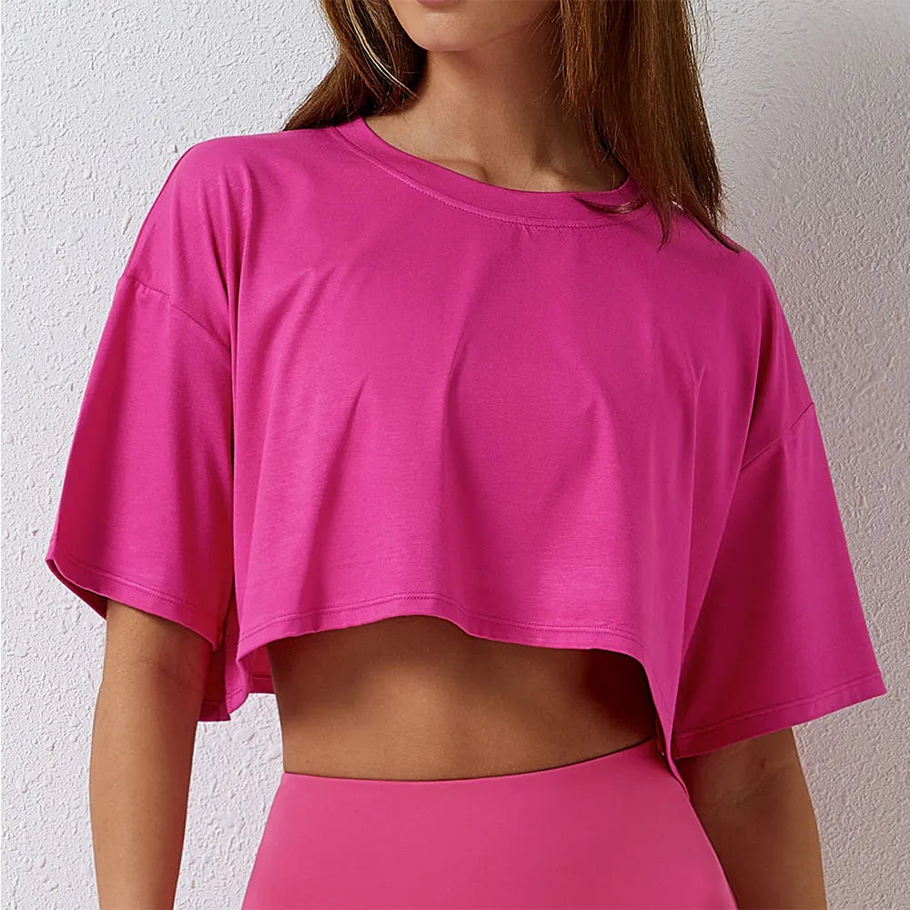 Woman wearing bright pink Luxe Crop Tee with short sleeves and crew neck, showing relaxed cropped fit and soft fabric texture